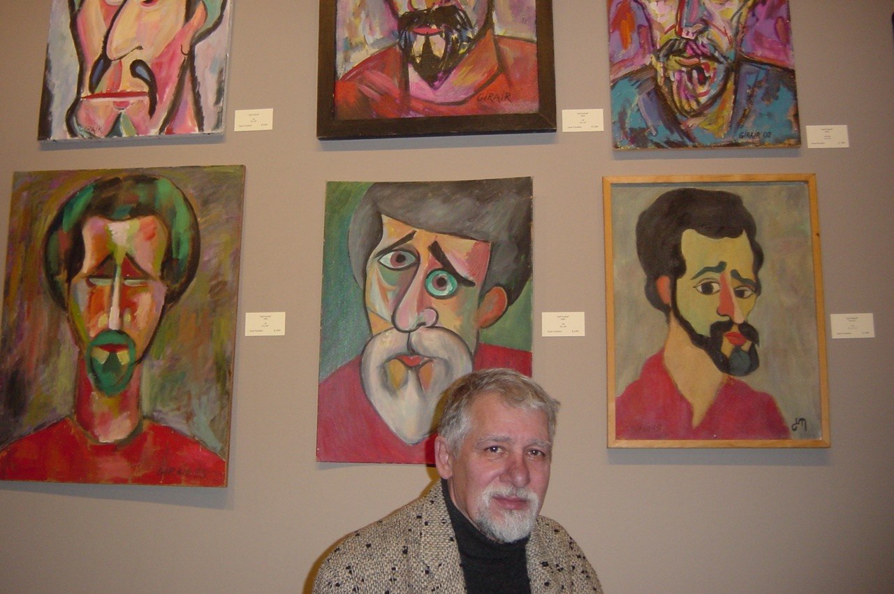 Girair Poladian seated beneath a display of his self-portraits